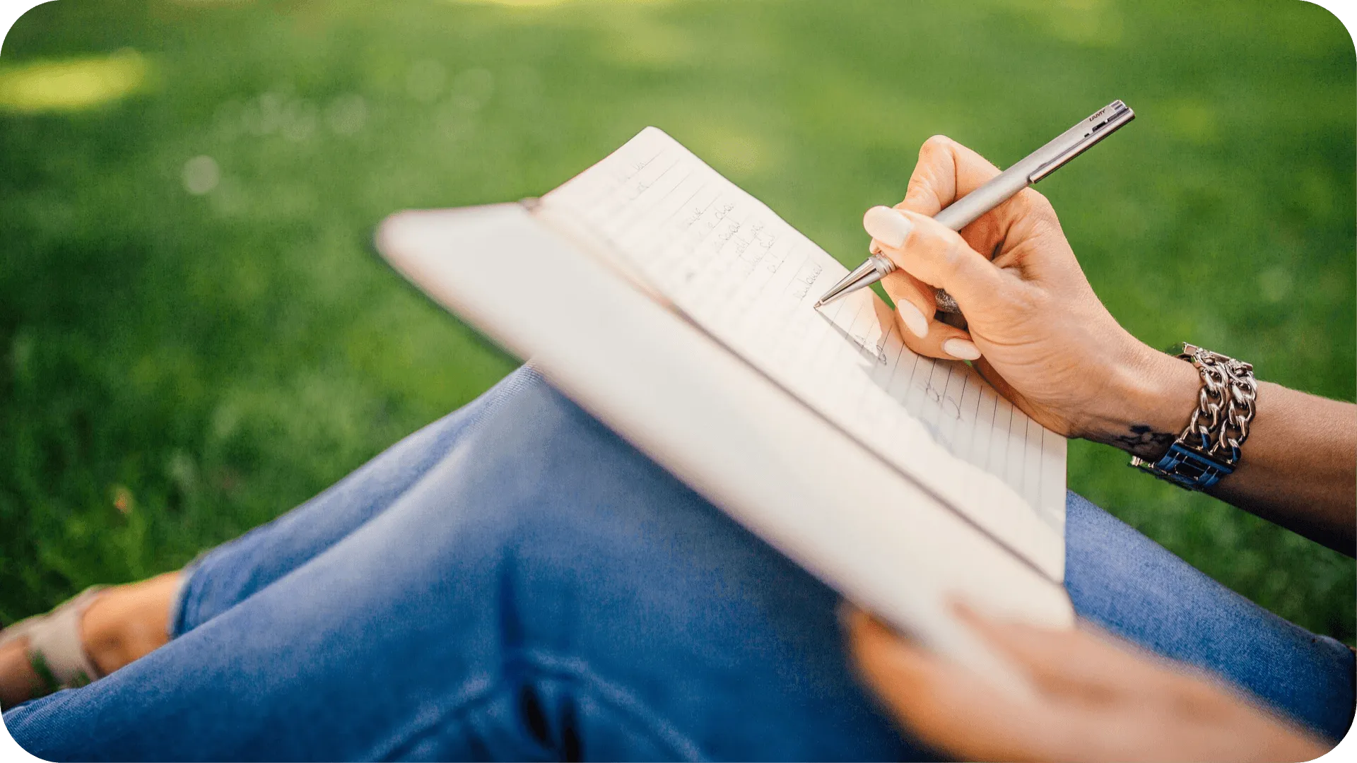 “Close up of a note book on a woman’s knee, while she writes some notes.”